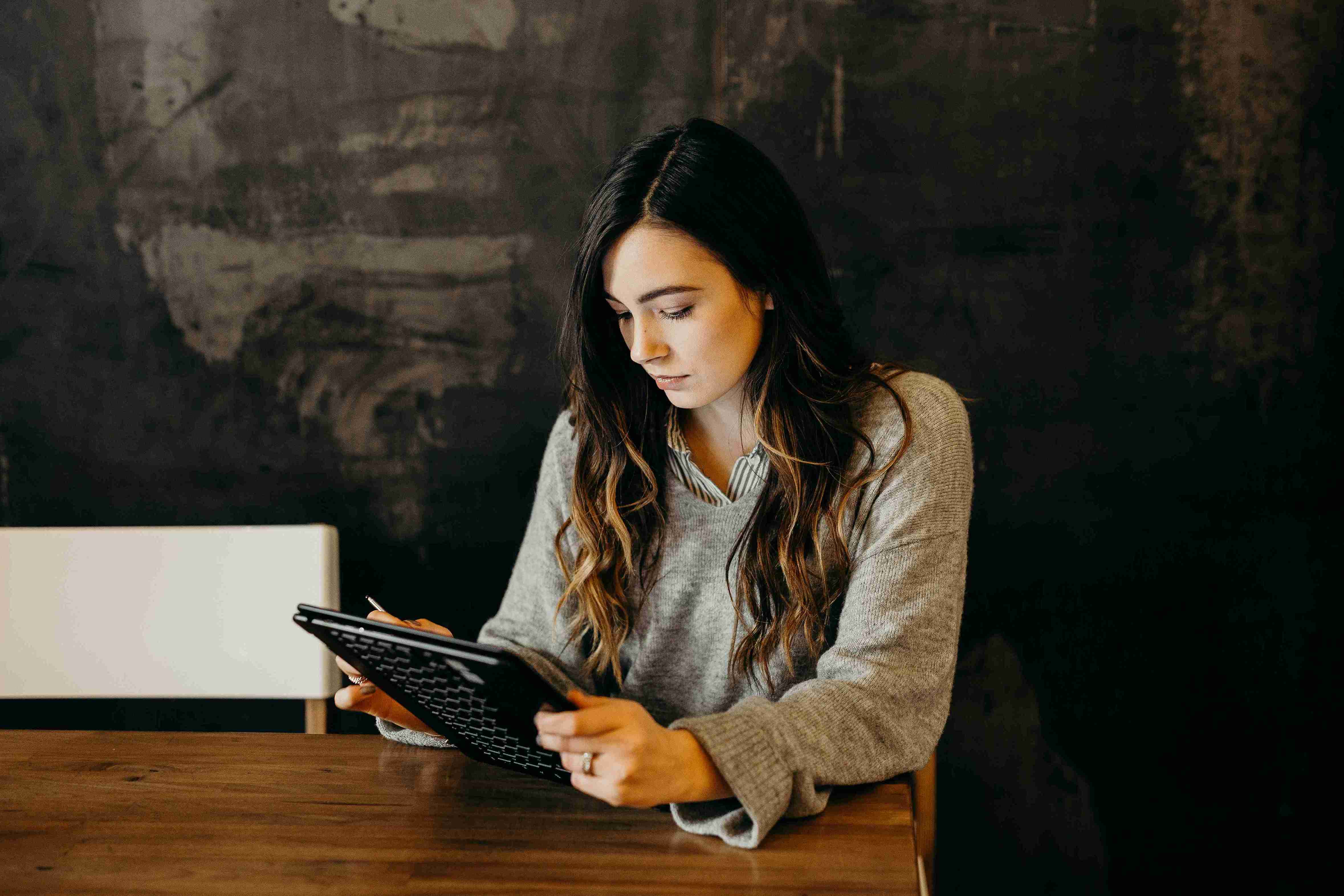 a lady with brown long hair sitting with an ipad in her hand at a table.